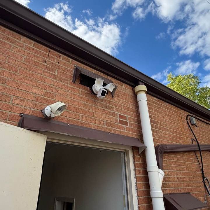 Floodlight security camera installed on a brick wall above a back entrance