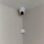 Indoor dome security camera in a ceiling corner with an alarm motion sensor below